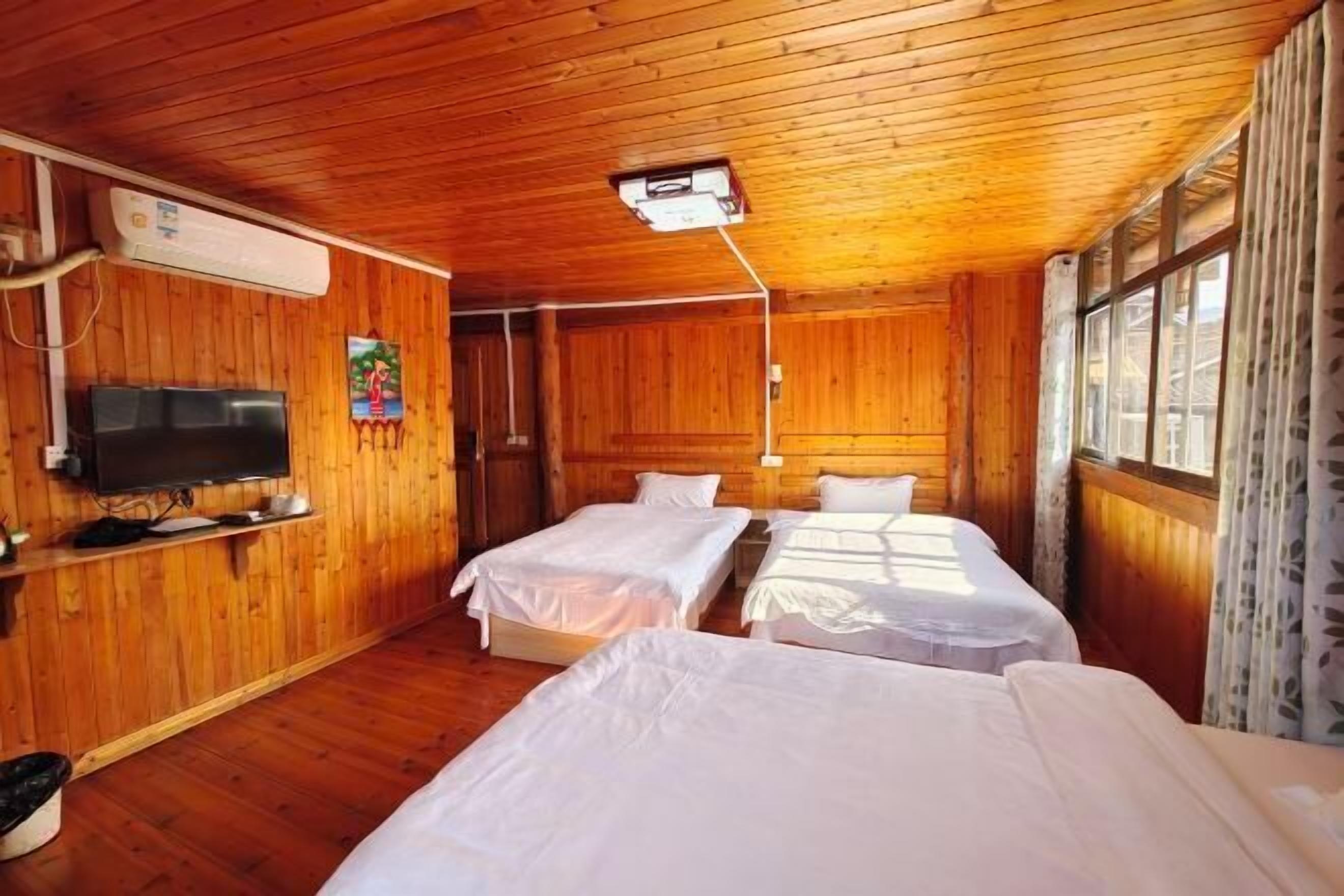 A room with wooden walls, a television, two beds, and a window.