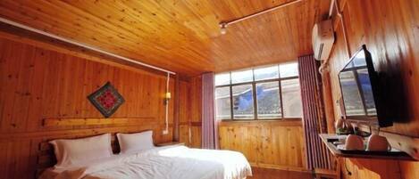 A wooden cabin room with a bed, a window, a TV, and a small table.