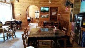 A wooden interior with tables and chairs, a television, and a refrigerator.