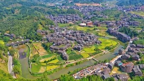 Vue aérienne d’un village avec ses bâtiments traditionnels, une rivière et la végétation luxuriante qui l’entoure.