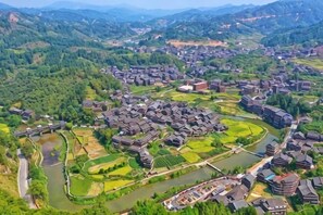 An aerial view of a village with traditional buildings, a river, and surrounding greenery. - Dongzhai Xiangfeng Inn (Sanjiang)