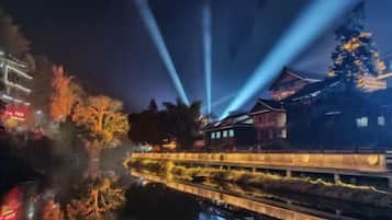 A nighttime view of a traditional building with illuminated beams, a river, and a bridge.
