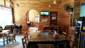 Un intérieur en bois comprenant un coin repas, des tables, des chaises, un téléviseur et un ventilateur.