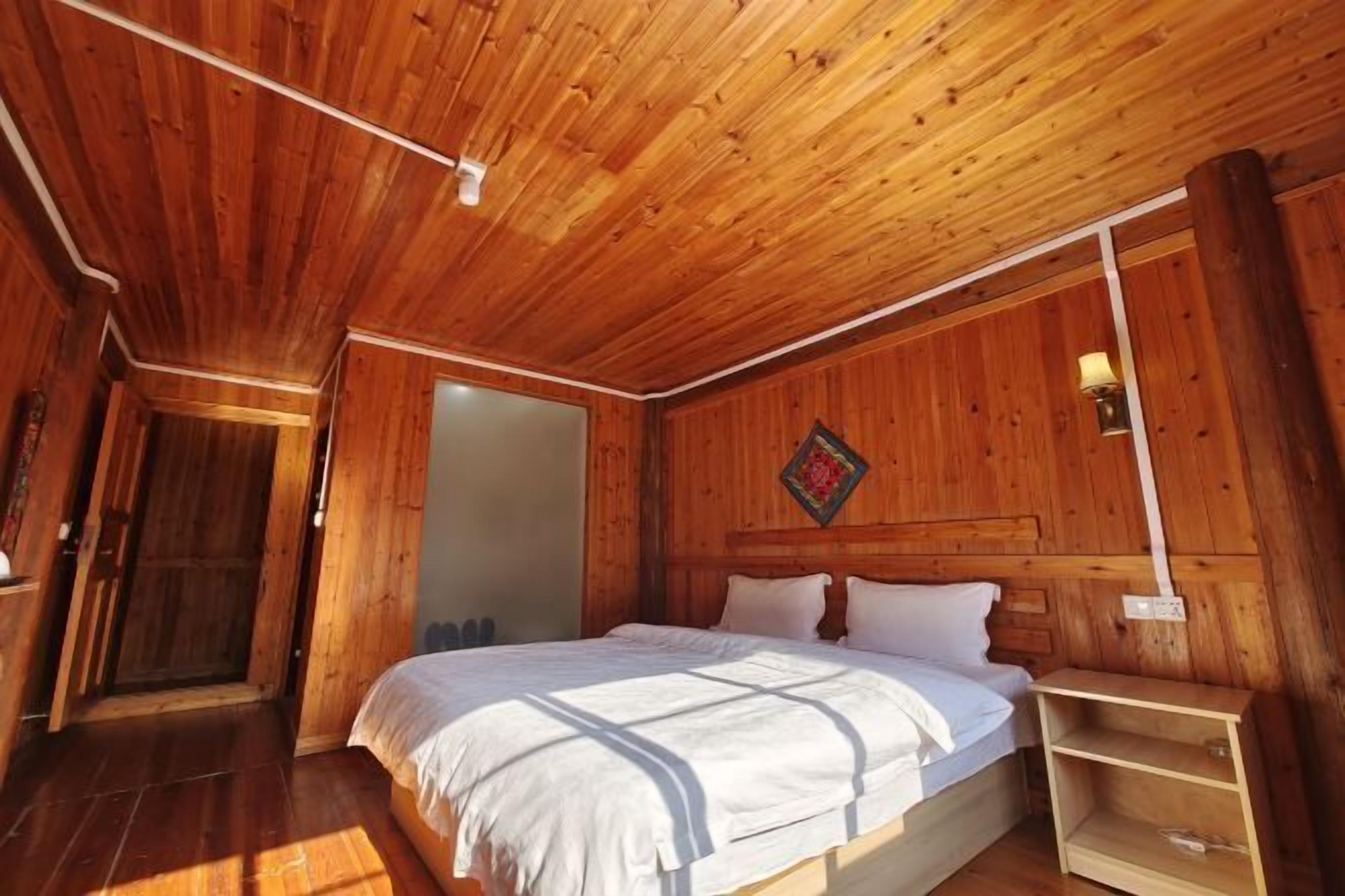 A wooden-paneled room with a bed, a nightstand, and a wall-mounted lamp.