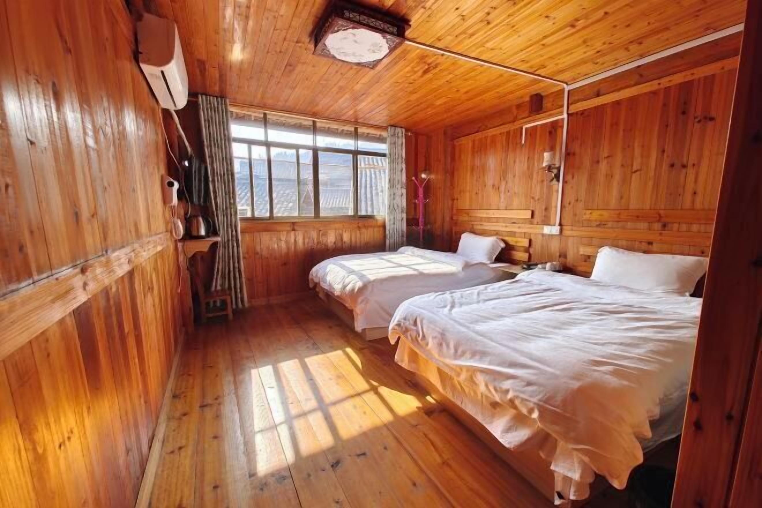 A wooden cabin room with two beds, a window, and a ceiling light fixture.