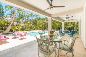 A covered outdoor area with a pool, lounge chairs, and a dining table with chairs.