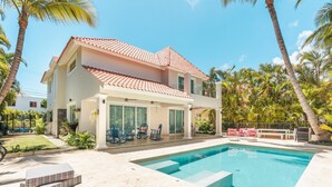 Une maison à deux étages avec une piscine, entourée de palmiers et d’une pelouse bien entretenue.