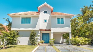 Une maison à deux étages, avec un toit recouvert de tuiles, une entrée centrale dotée d’une porte bleue et un petit porche.