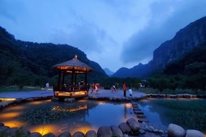 Un belvédère doté d’un toit et d’une balustrade, entouré d’une étendue d’eau paisible, avec des montagnes en arrière-plan.