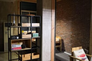 Une pièce avec un mur en briques, une étagère noire contenant divers objets et une chaise en bois.