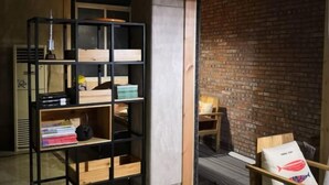 Una habitación con pared de ladrillo, una estantería de madera, una silla de madera y una pequeña mesa con lámpara.