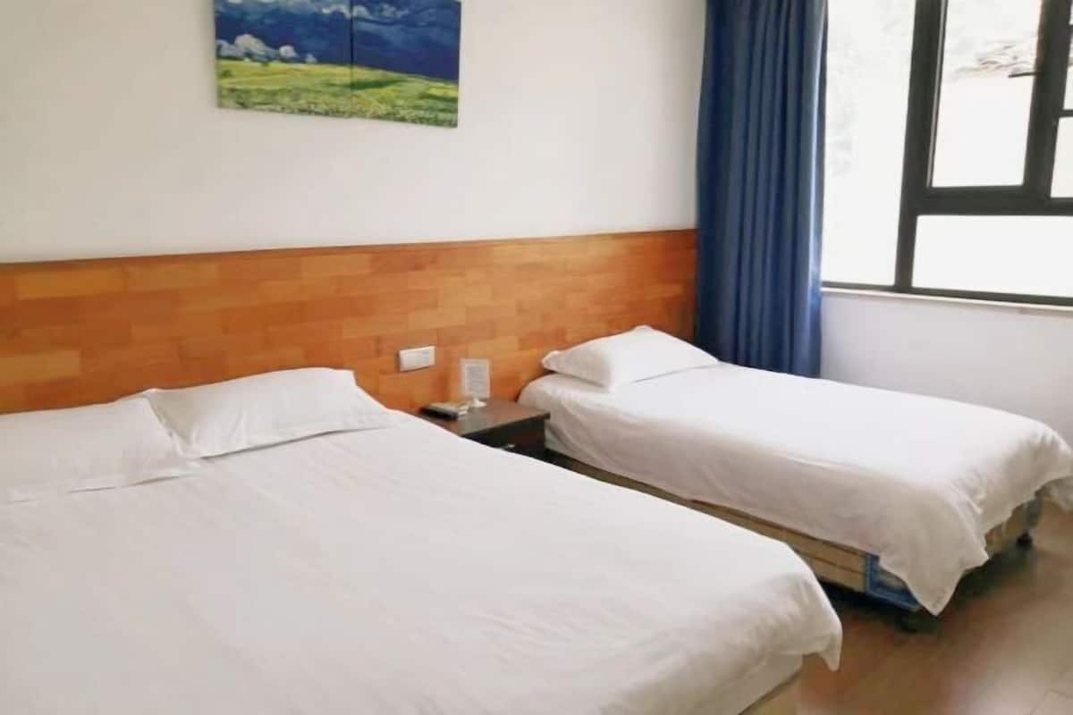 Una habitación con dos camas, cabecero de madera, mesita de noche, un cuadro y una ventana con cortinas.