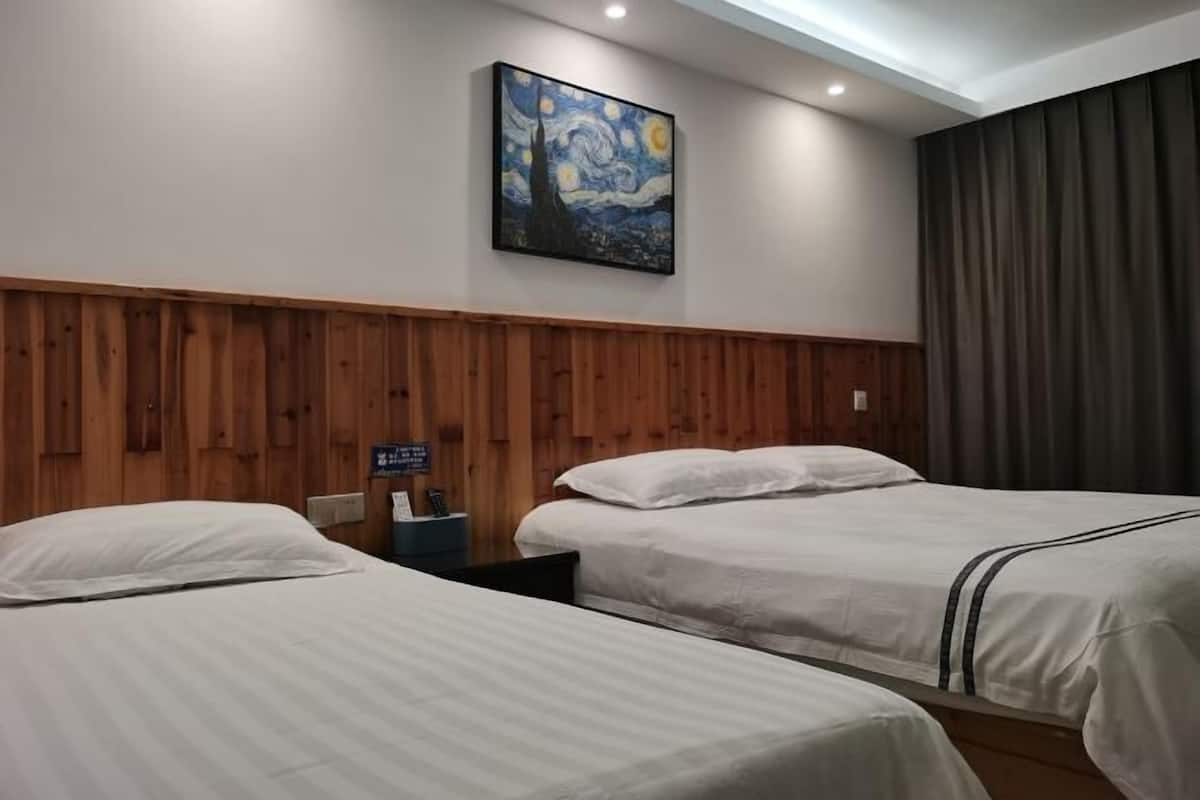 Habitación de hotel con dos camas, paneles de madera en las paredes, un cuadro sobre las camas y una cortina oscura en la ventana.