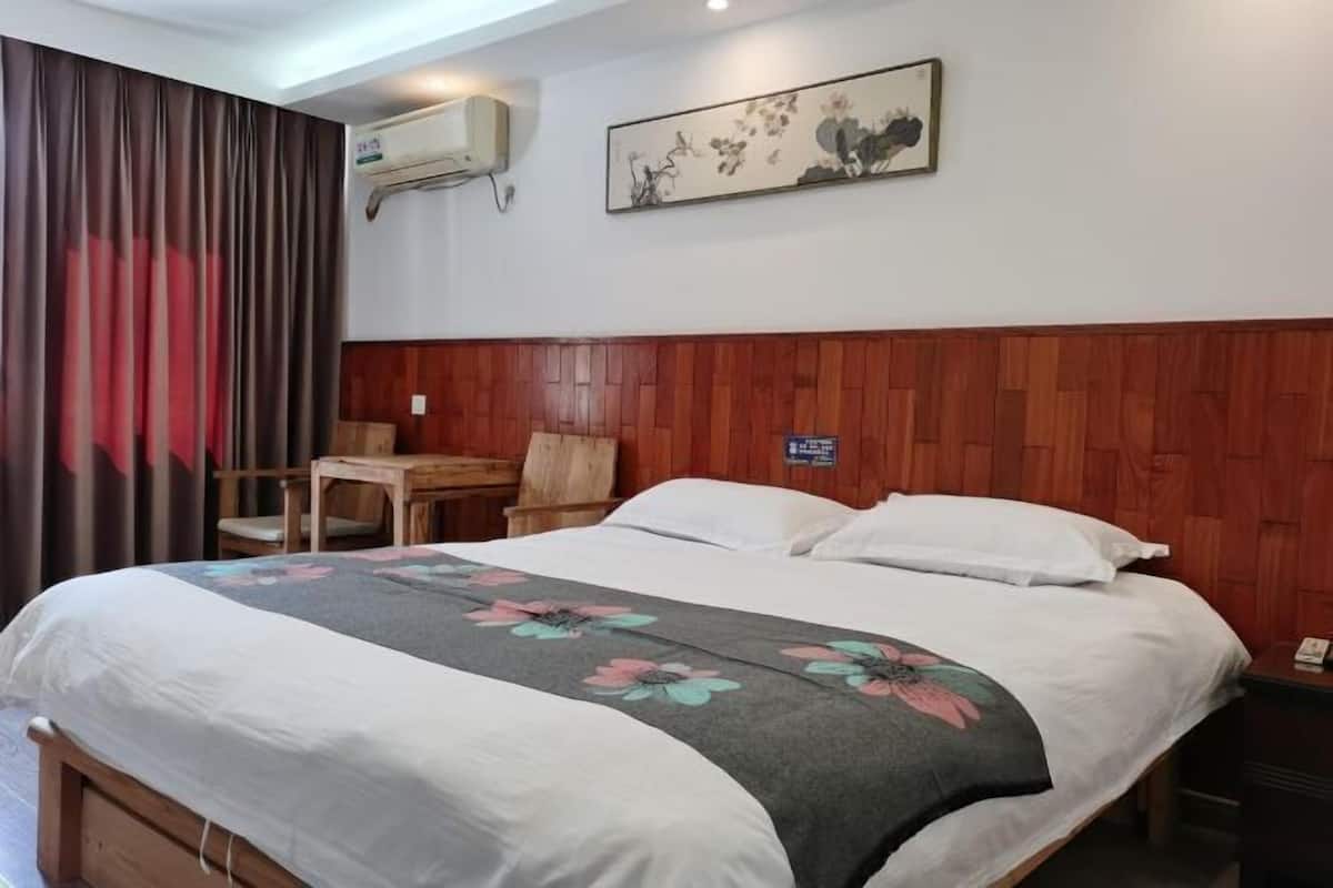 Habitación de hotel con cabecera de madera, cama con colcha estampada, escritorio con silla y aire acondicionado de pared.