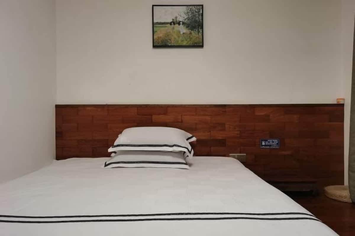 Una cama individual con cabecera de madera, ropa de cama blanca con rayas negras y un cuadro en la pared.
