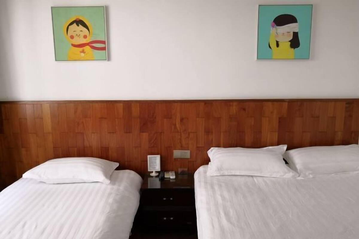 Habitación de hotel con dos camas, cabecero de madera, ropa de cama blanca y dos obras de arte colgadas en la pared.