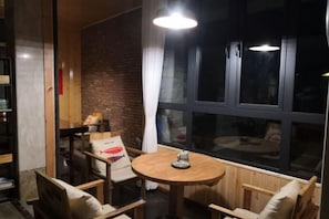 Une pièce avec une table ronde en bois, deux chaises, un mur en briques et une grande fenêtre.