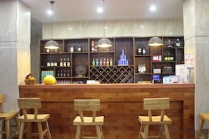 Un espace bar avec des tabourets en bois, un comptoir où sont exposées différentes bouteilles et un éclairage suspendu.