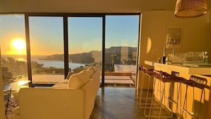 Een moderne keuken met een groot raam met uitzicht op een schilderachtige waterpartij en heuvels bij zonsondergang.