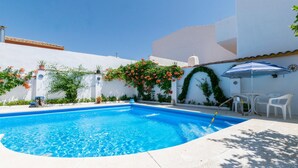 Una piscina con agua azul cristalina, rodeada de muros blancos y vegetación.
