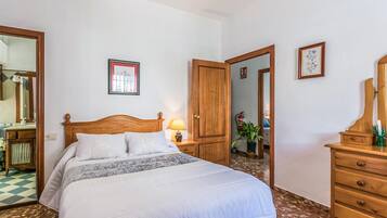 Une chambre d’hôtel bien rangée, avec un lit en bois, une table de chevet avec une lampe, une commode et un miroir.