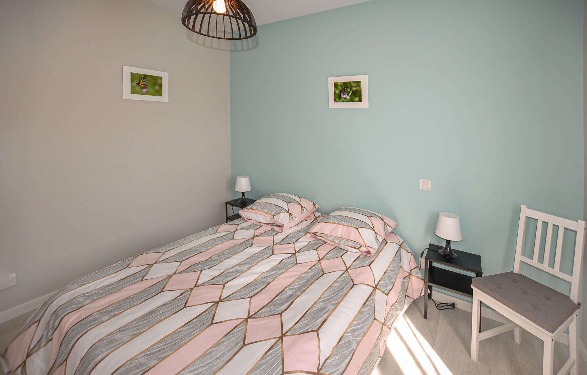 A bedroom with a bed, two bedside tables, a chair, and two wall-mounted pictures.