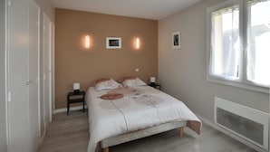 Un dormitorio con cama, mesitas de noche, luces en la pared, un radiador y una ventana.