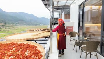 A person tending to a large tray of food on a balcony with a view of mountains.