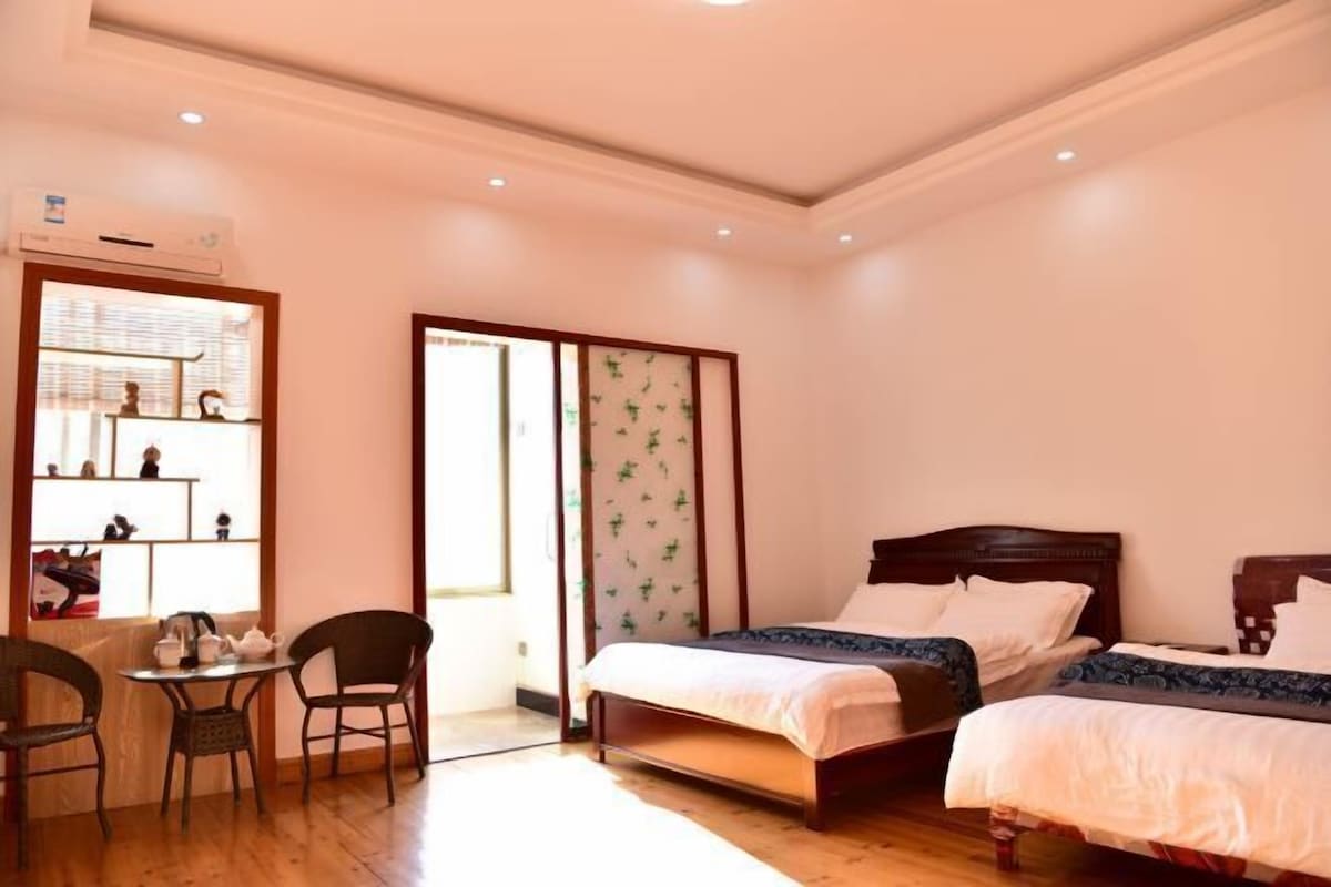 A room with two beds, a small table with chairs, and a sliding door leading to a balcony.