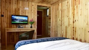 A wooden-paneled room with a bed, a desk, and a television. - Huangjia Inn (Wuyuan)