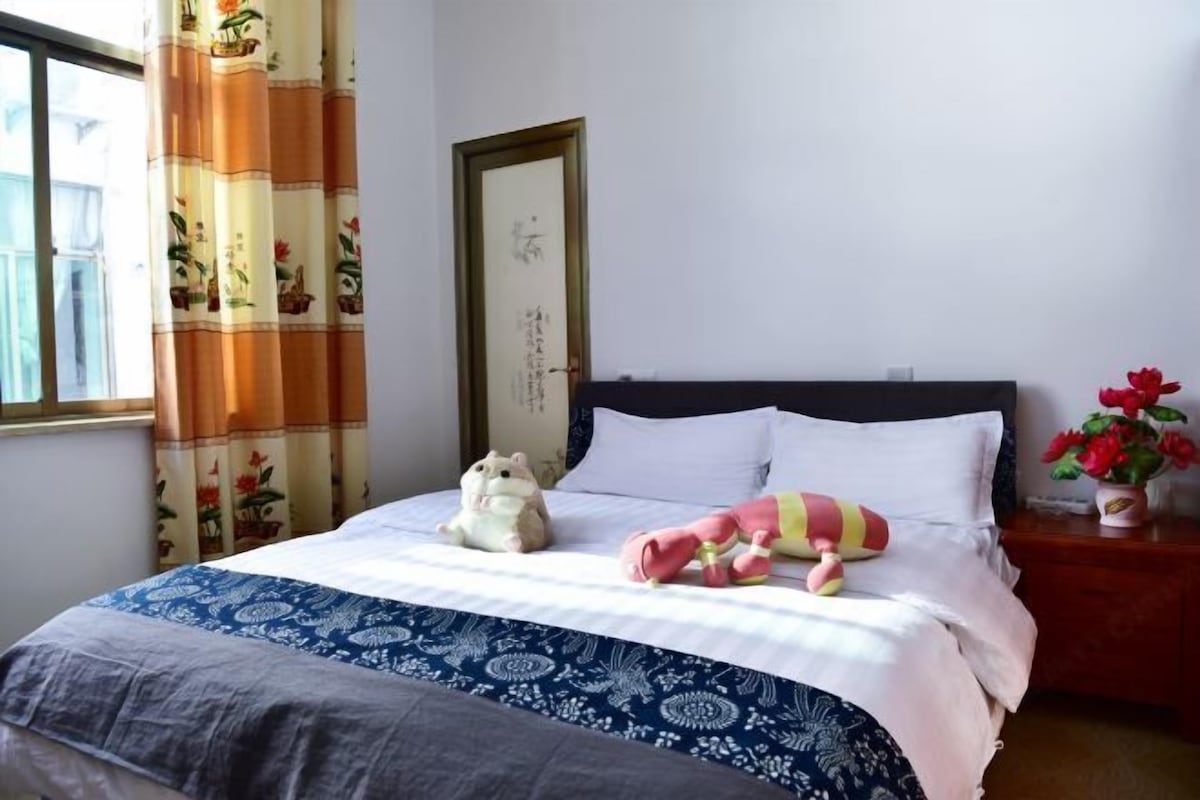 A neatly made bed with a blue and white patterned bedspread, a small stuffed animal, and a decorative pillow.