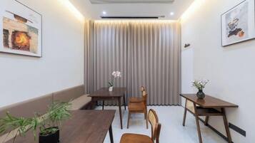 A hotel room with a wooden dining table, chairs, a potted plant, and a curtain-covered window.