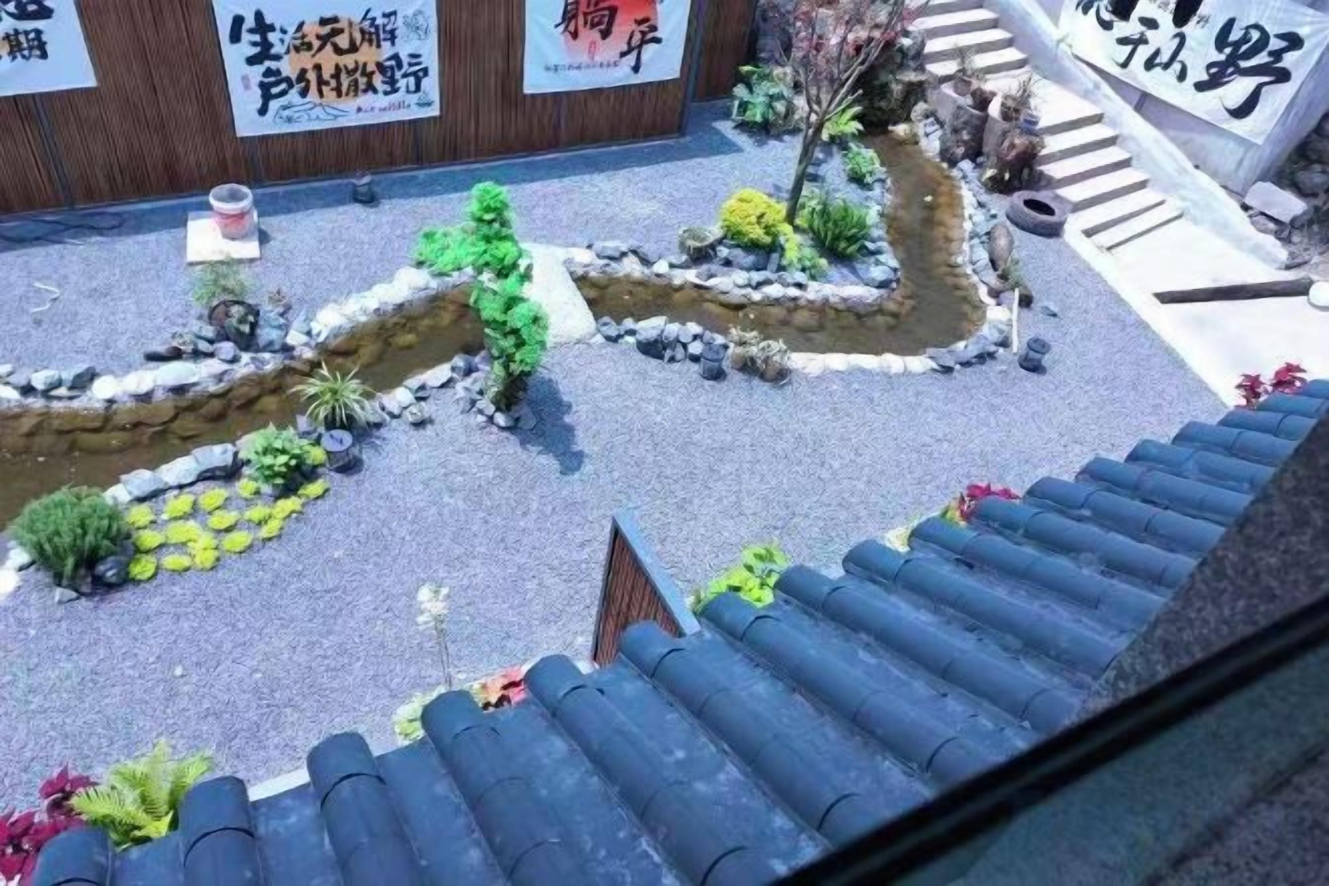 A courtyard with a small stream, potted plants, and a traditional tiled roof.