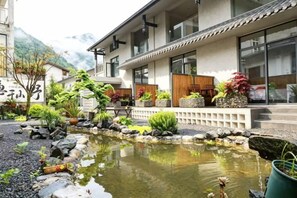 A traditional Japanese building with a koi pond, potted plants, and a stone pathway.