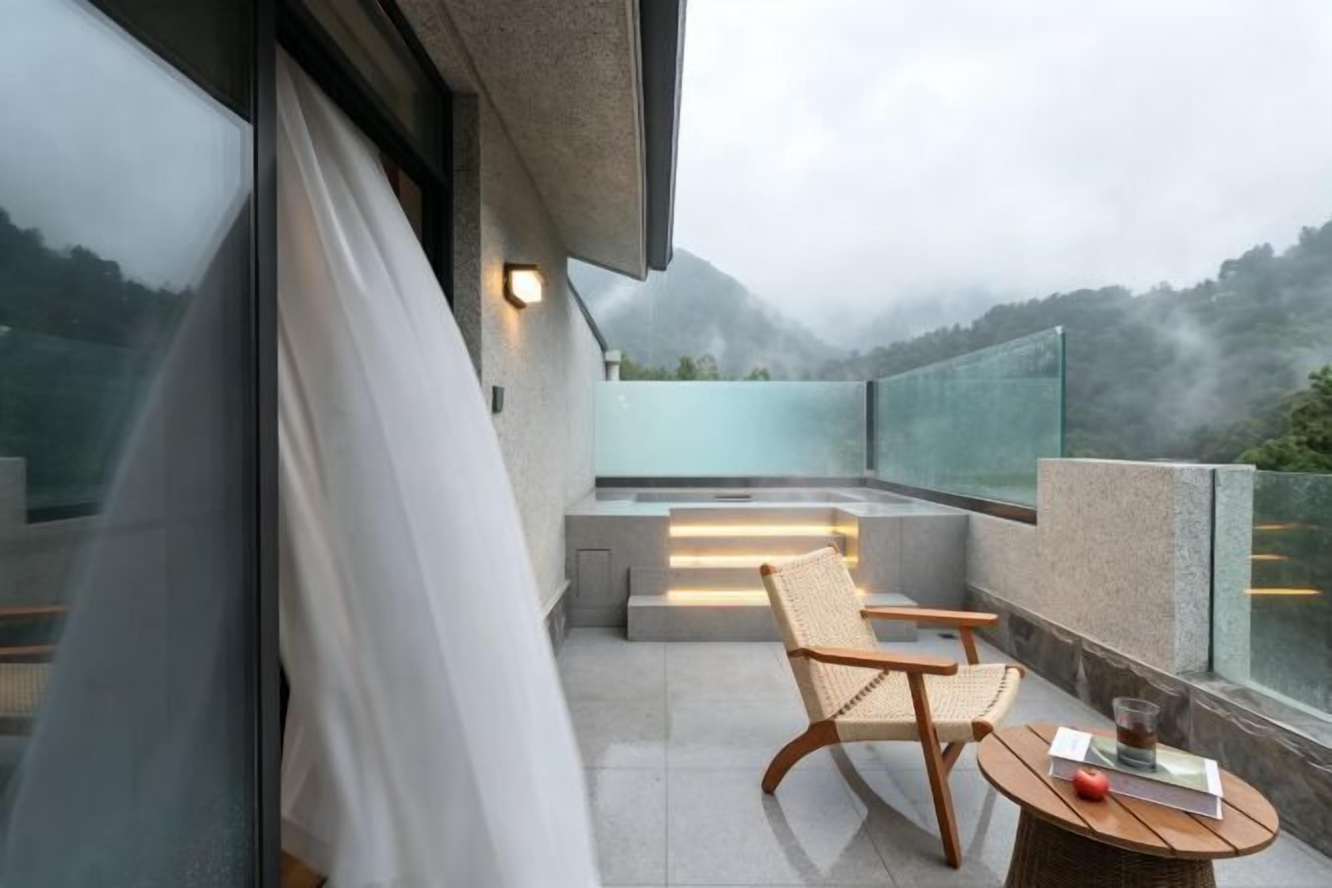 A balcony with a chair and table, overlooking a mountainous landscape.