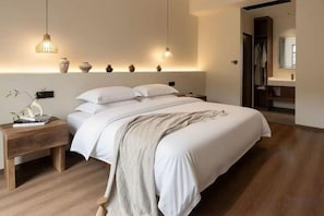 A bedroom with a large bed, bedside tables, and a nightstand. There are wall-mounted lights and a mirror above the bed.