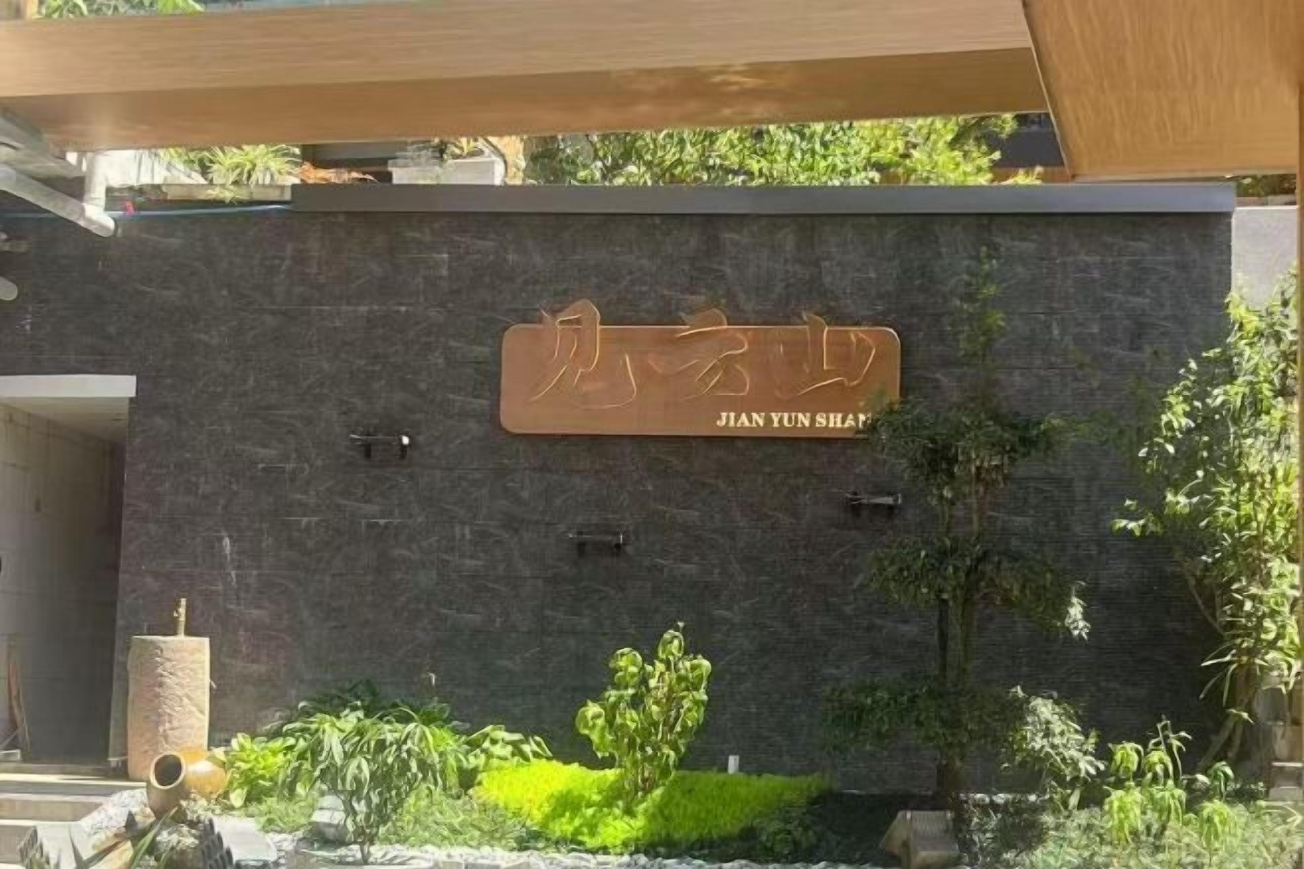 Fachada moderna de un edificio con un letrero que dice 'JIAN YUN SHEP' y un pequeño jardín con plantas y una fuente.