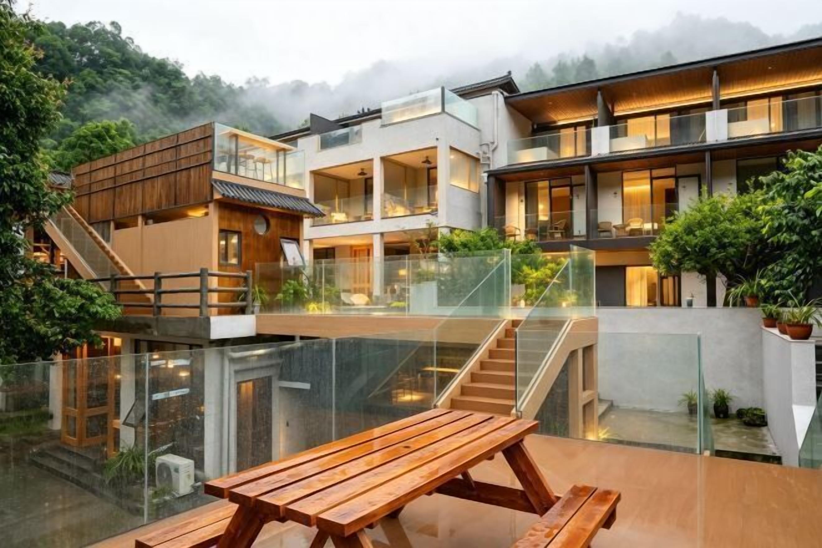 Un edificio moderno de varios pisos con barandas de vidrio, bancos de madera al aire libre y una escalera que sube a niveles superiores.