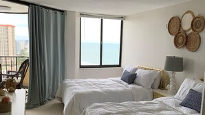 Hotellihuone, jossa on kaksi sänkyä, parveke, jolta on näkymä merelle, ja seinä, joka on koristeltu punotuilla koreilla.