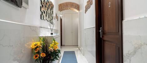 A hotel corridor with a marble floor, a blue carpet, a wooden door labeled "FARO SUITE 2", and a wall-mounted artwork.