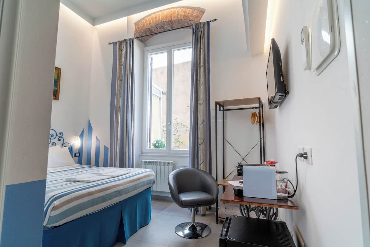 Une chambre d’hôtel avec un lit, un bureau avec un ordinateur portable, une chaise et une fenêtre avec des rideaux.