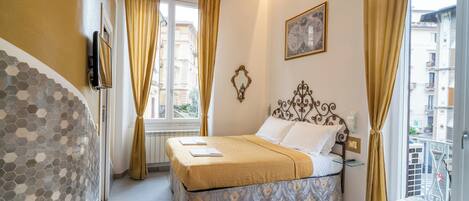 A hotel room with a bed, a window with curtains, a wall-mounted picture, and a patterned floor.