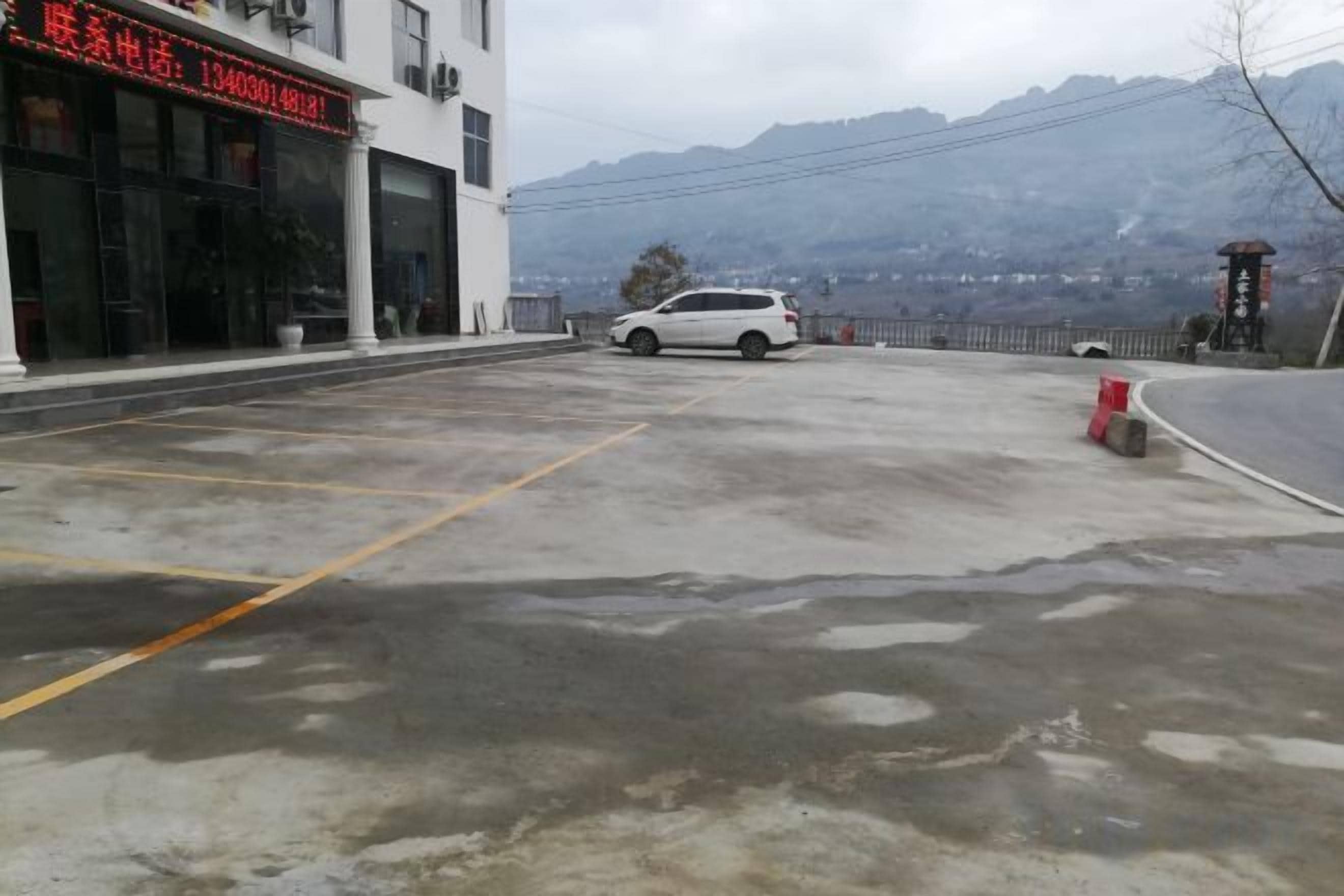 Un espace de stationnement avec une voiture blanche, un bâtiment avec une enseigne rouge et des montagnes en arrière-plan.