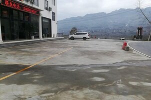 A parking area with a white car, a building with a red sign, and mountains in the background.