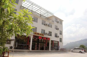 Un edificio de varios pisos con fachada comercial en la planta baja, unidades de aire acondicionado y un vehículo estacionado al frente.