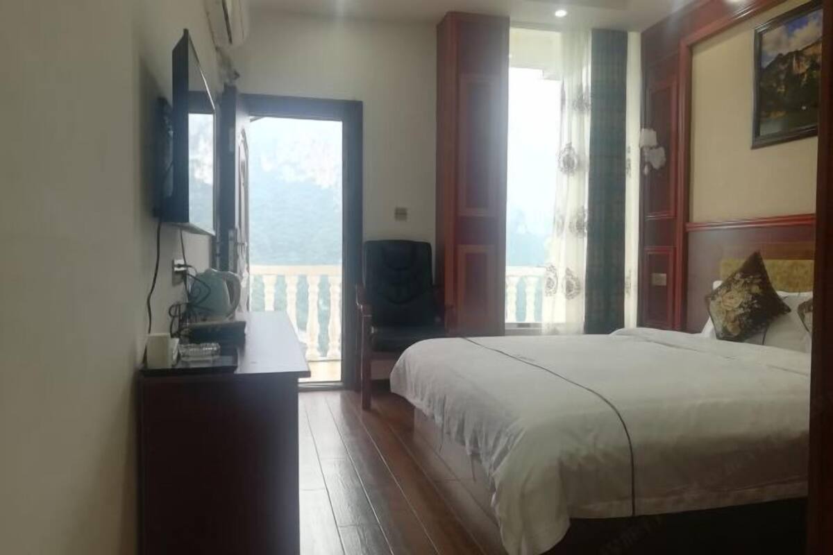 Un dormitorio con cama, televisión sobre un mueble bajo, cómoda de madera y balcón con vistas.