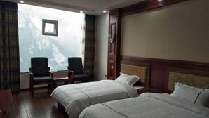 A hotel room with two beds, a small table, two chairs, a window with a mountain view, and a wooden headboard.