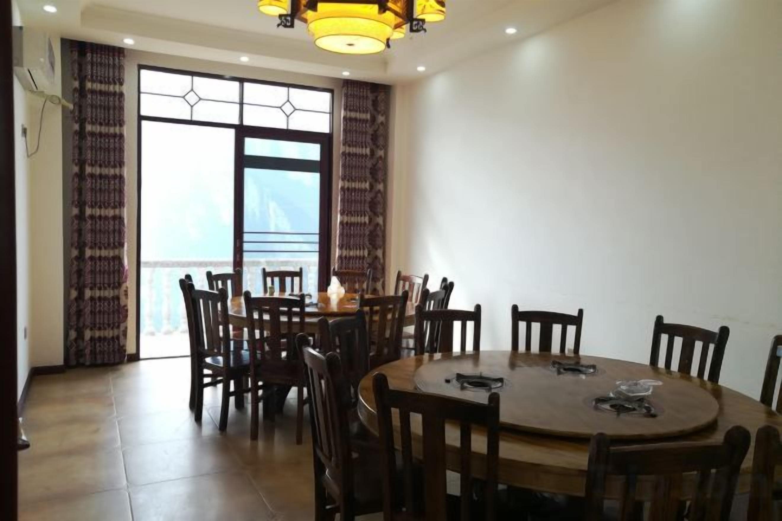 A dining area with a round table and chairs, a chandelier, and a view through a large window.