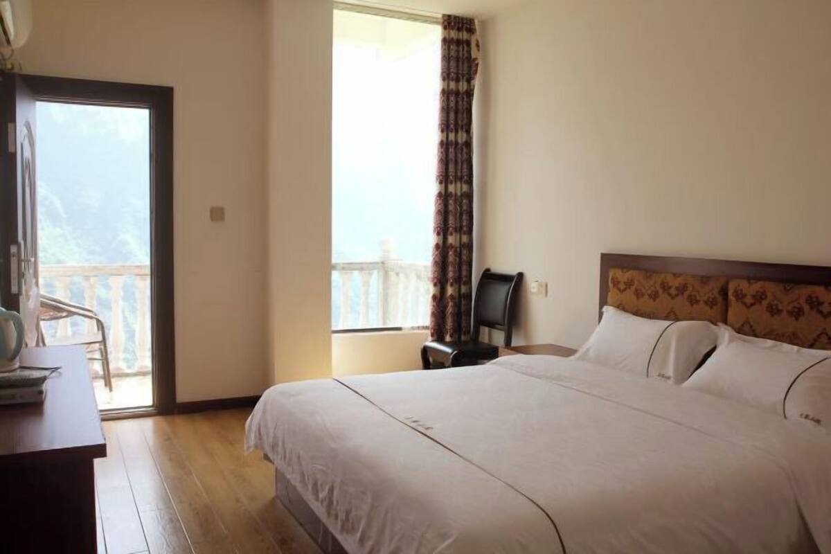 Habitación de hotel con cama, escritorio, silla, ventana con cortinas y balcón.