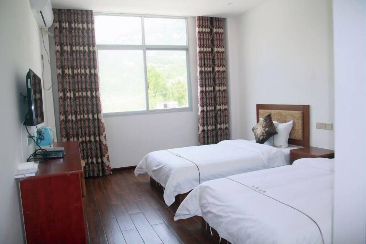 Una habitación de hotel con dos camas, un escritorio, un televisor y una ventana con cortinas.